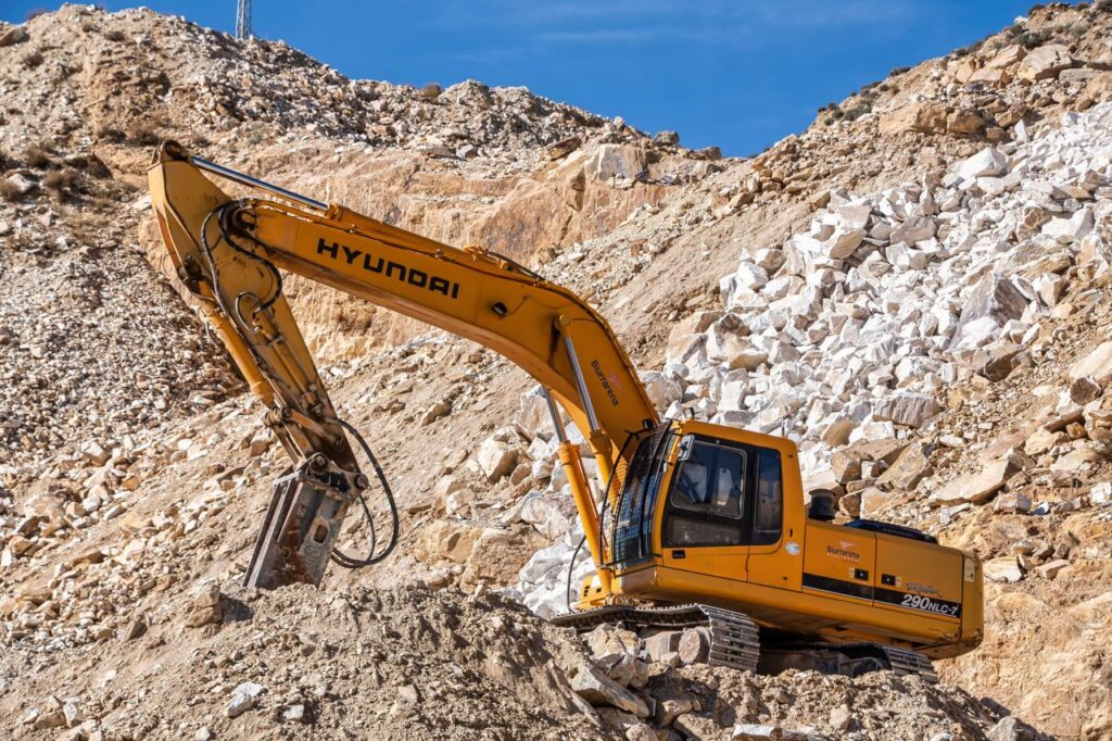 Yellow Hyundai excavator operating in a rocky quarry under a clear blue sky. Perfect for industrial themes.